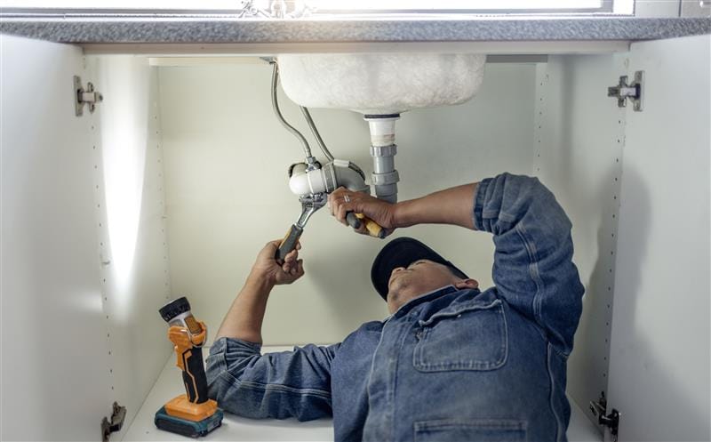 Plumber repairing pipes beneath a bathroom sink in Winter Garden