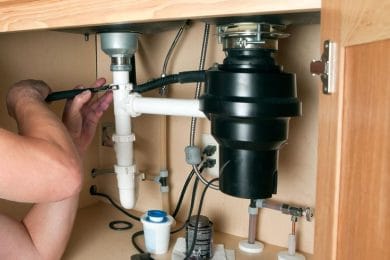 Plumber repairing a garbage disposal beneath a kitchen sink in Winter Garden